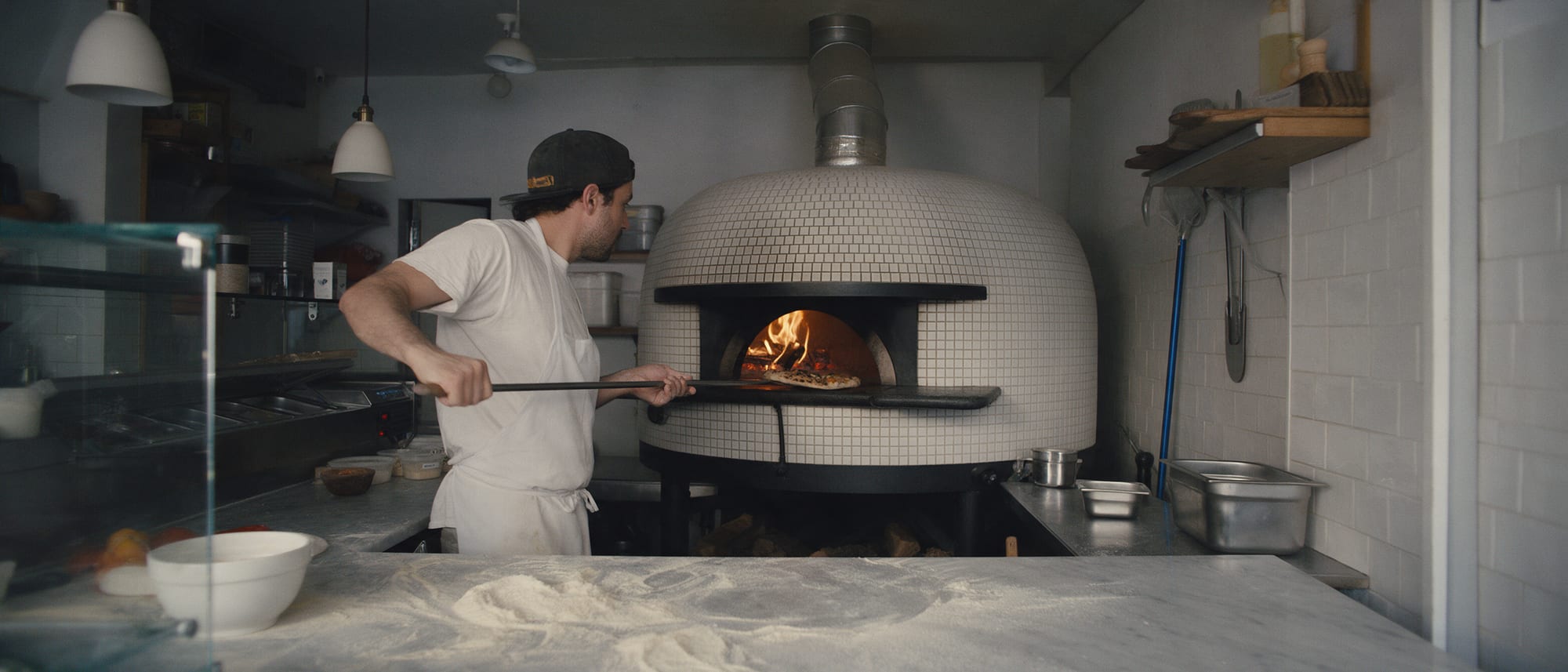 Le pizzaiolo enfourne une pizza dans le four à bois carrelé de blanc