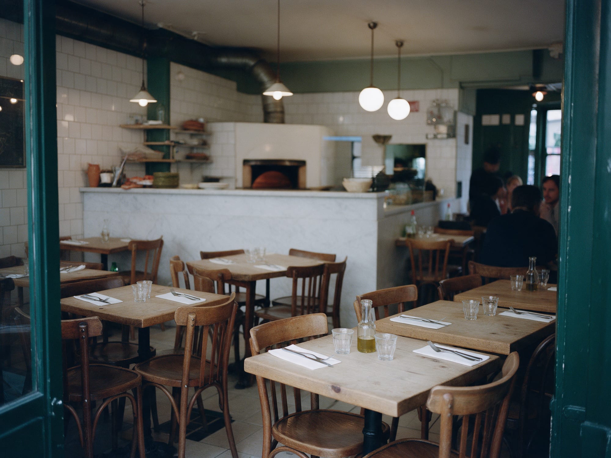 La salle : tables en bois, chaises bistrot, comptoir en marbre et four au fond